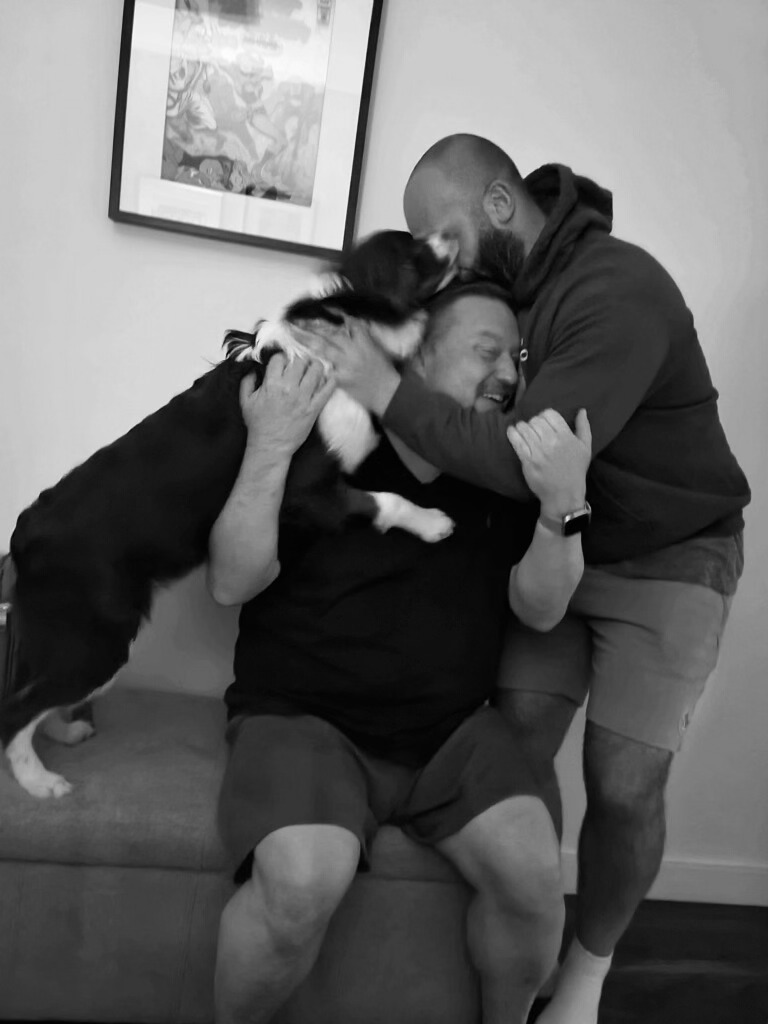 dog and two men, owners of the property in one embrace